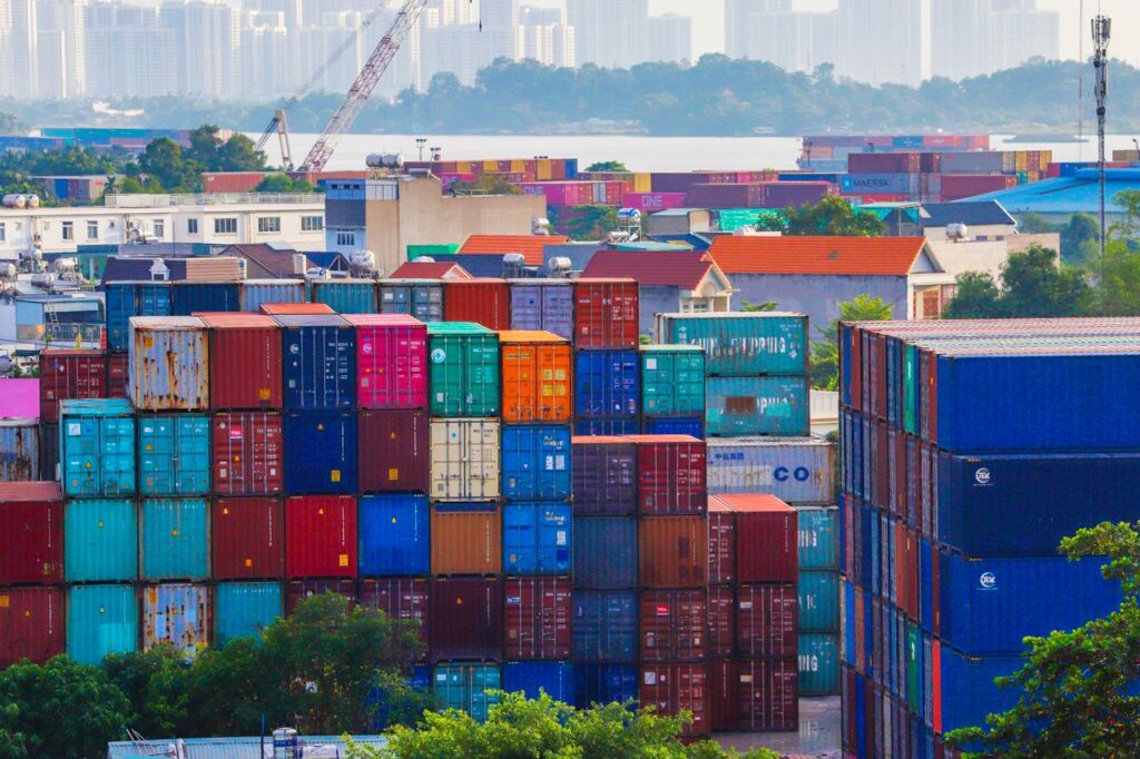 pexels photo 33401363 Vibrant stacked cargo containers at a bustling port with urban skyline in background.
